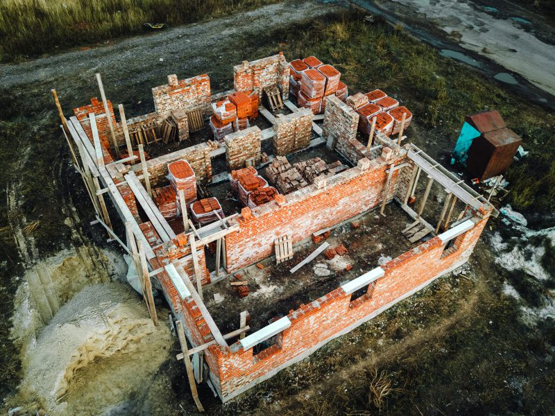Luftaufnahme der Baustelle für zukünftiges Backsteinhaus, Betonfundamentboden und Stapel von Gelb